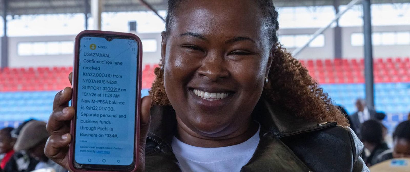A young NYOTA business support beneficiary smiles and holds up her phone.